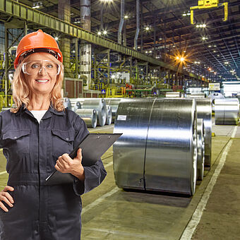 Industrial worker standing in front of steel coils while holding documents, symbolizing local production systems and optimized decentralized manufacturing.
